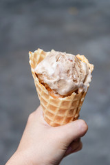 Woman hand holding melting coffee almond flavor ice cream in waffle cone.