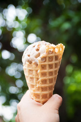 Woman hand holding melting coffee almond flavor ice cream in waffle cone.
