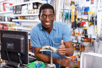 Portrait of happy successful owner of household goods store standing behind counter, giving thumbs...