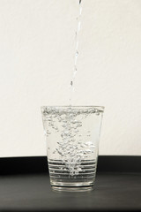 Pouring water into a glass on black table; health and diet concept.  