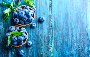 Bowl of fresh blueberries on blue rustic wooden table from above.