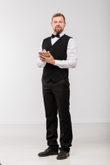 Young elegant waiter with notepad and pen writing down order of one of clients