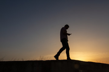 silhouette of man with cell phone at sunset