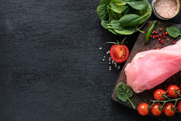Raw turkey fillet ready for grilling. Chicken fillet on a wooden cutting board with cherry tomatoes, hot pepper, spinach leaves and greens. copy space. top view.