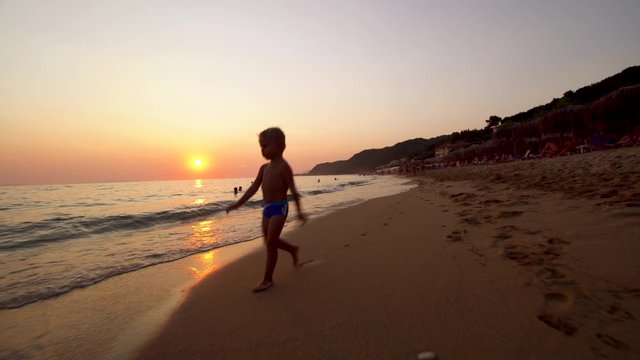 Baby Boy Running On A Sand Beach Toward The Camera At Sunset