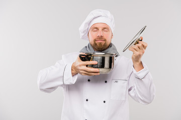 Young professional chef enjoying nice smell of soup or other cooked meal in pan