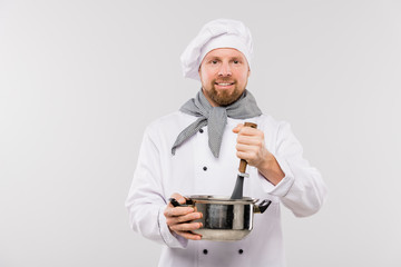 Professional male chef mixing soup or other meal in pan while cooking food