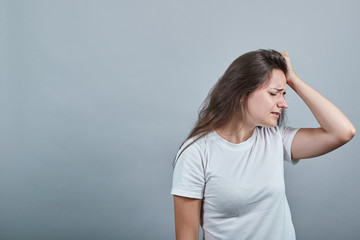 Young lady in white t-shirt over isolated wall holds her palm on her head, she has headache. Girl looks sad, unhappily and worried