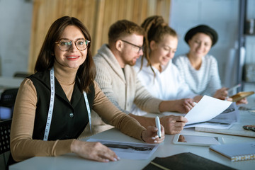 Pretty young fashion designer drawing new sketch on background of colleagues