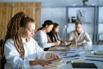 Pretty young fashion designer with color palette working by desk in studio