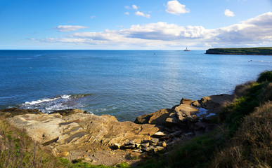 Fototapeta na wymiar The rocky coastline of Seaton Sluice with St Mary's Lighthouse out at sea in the distance.