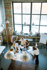Group of contemporary creative designers gathered by table in studio