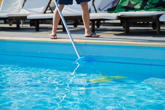 Male cleaning outdoor swimming pool with underwater vacuum tube