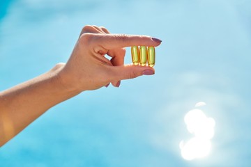 Sunny golden vitamin D oil capsules Omega-3 in woman hand