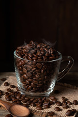 Roasted coffee beans in a clear cup of coffee on burlap and wood. Dark mood coffee beans photography.