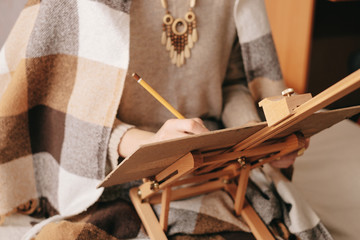 Woman artist drawing on paper easel with pencil.