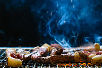 Raw Meat beef sliced bbq grilling on rack charcoal stove with smoke and fire on black background.