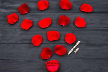 Dark wooden textured floor background covered with red rose petals. Close up, top view, copy space