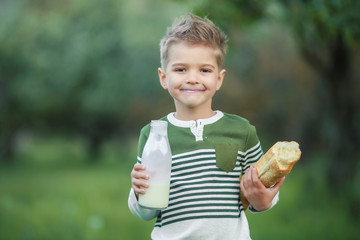 Little boy with girl drink milk and eat a loaf of bread on a haystack in a village at sunset.
