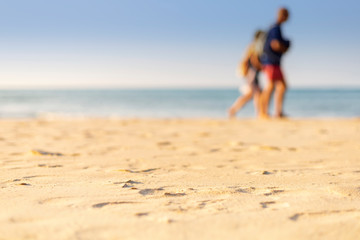 Fototapeta premium Holiday concept. Clear sand with blur guy, sea and clear sky background. Soft focus and focus selective sand.