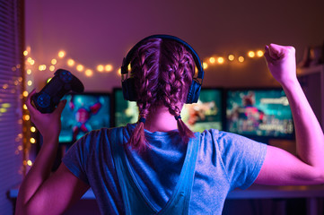 Gaming and e-sports. A streamer girl plays games using the joystick and gamepad. On three monitors, creative light © Anton