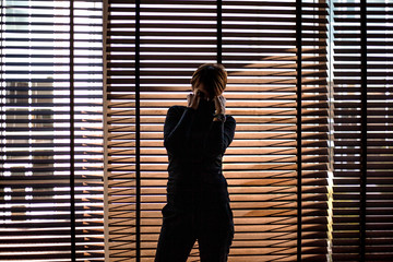 Silhouette of a beautiful 45s years old woman in black style clothes on a background of jalousie indoors at the house.