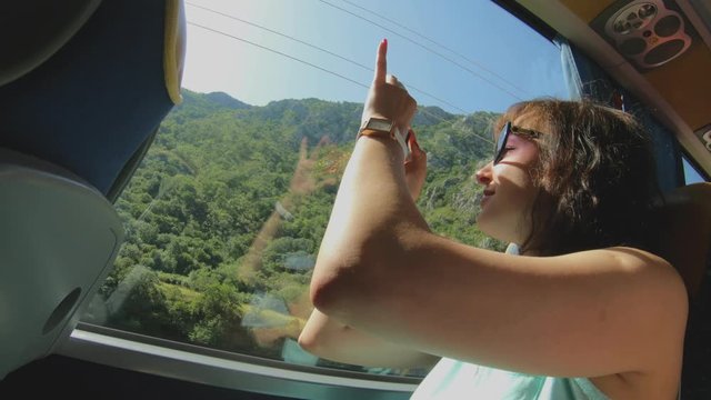 Tourist girl with smartphone takes pictures of nature landscape through bus window. Sightseeing trip and Travel. Vacation in Montenegro, excursion