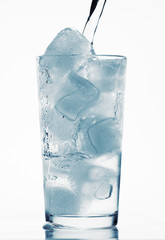 pouring water in a glass full of ice cubes, white background, blue toned object