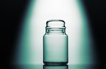 Empty glass jar on a green, black and white background with light effect