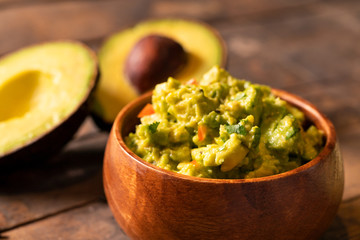 Close-up of spicy guacamole dip bowl and avocados in the background