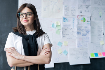 Pretty young businesswoman in eyeglasses crossing arms by chest