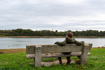young boy sitting on the bench by the lake