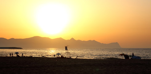 the sun setting behind the promontory with the sea in the foreground