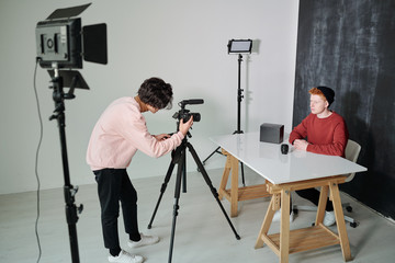 Young cameraman bending in front of video shooting equipment in studio