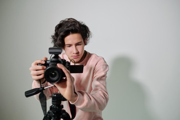 Young cameraman in powdery pink sweatshirt regulating video equipment