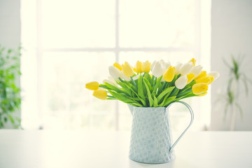 A bouquet of tulips in a pot in the form of a teapot on a white table. Taken in warm daylight.