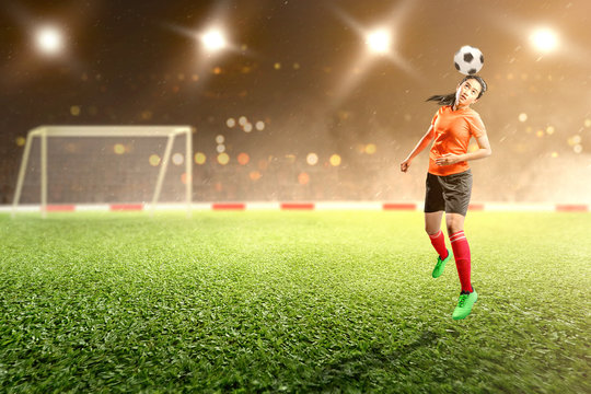 Asian football player woman jump and heading the ball on the air on the football field - Powered by Adobe