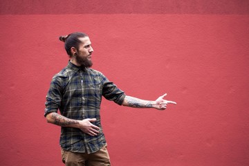 young man with beard and gauged pierced ears pointing in front of a red wall background