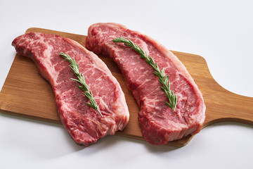 Raw beef steak ready to be cooked. Photo of two fresh raw striploin steak on wooden board on white background with rosmary.