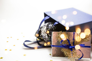 Christmas composition - blue paper bag with golden box gifts with blue bow ribbon, Xmas bauble, balls on white background with stars, lights. 