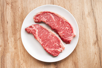 Striploin steaks being prepared for cooking Photo of two fresh raw striploin steak on white plate. Raw juicy beef steak ready to be cooked. Top view food preparation process concept.