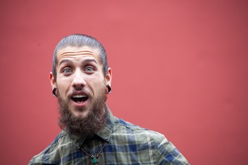 young man with beard and gauged pierced ears on red wall background