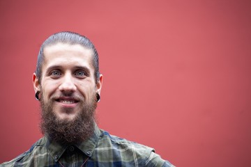 young man with beard and gauged pierced ears on red wall background