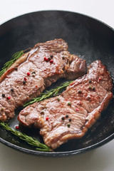 Frying pan, steak, cooking on fire concept. Steaming, reeky, flavored spicy grilled beef striploin steak in a frying pan on a white background.