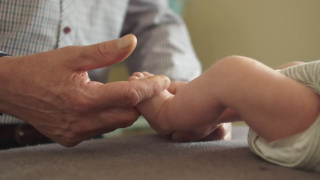 Grandfather tickling the very tiny feet of the newborn. Slow-motion close up shot of the wrinkled hands playing with the little baby