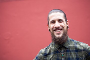 young man with beard and gauged pierced ears on red wall background