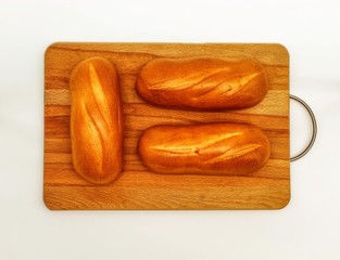 Three small fresh loaves of white bread lie on a wooden Board