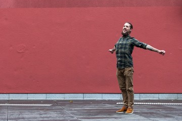 young man with beard and gauged pierced ears jumping in front of red wall background