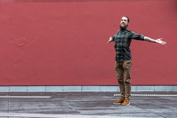 young man with beard and gauged pierced ears jumping in front of red wall background