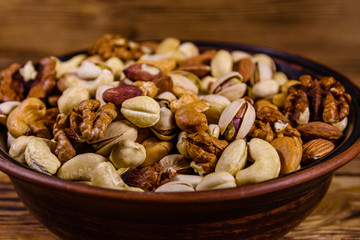 Various nuts (almond, cashew, hazelnut, pistachio, walnut) in ceramic plate on a wooden table. Vegetarian meal. Healthy eating concept